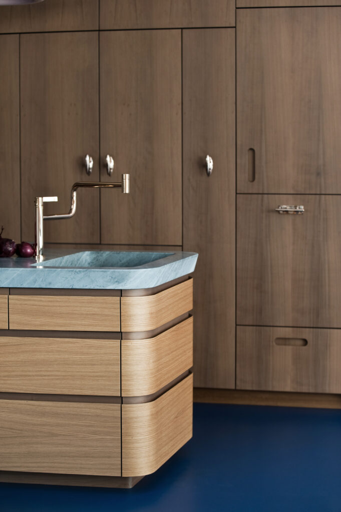 Detailansicht einer Holzschrankwand mit blauer Arbeitsplatte und goldener Armatur